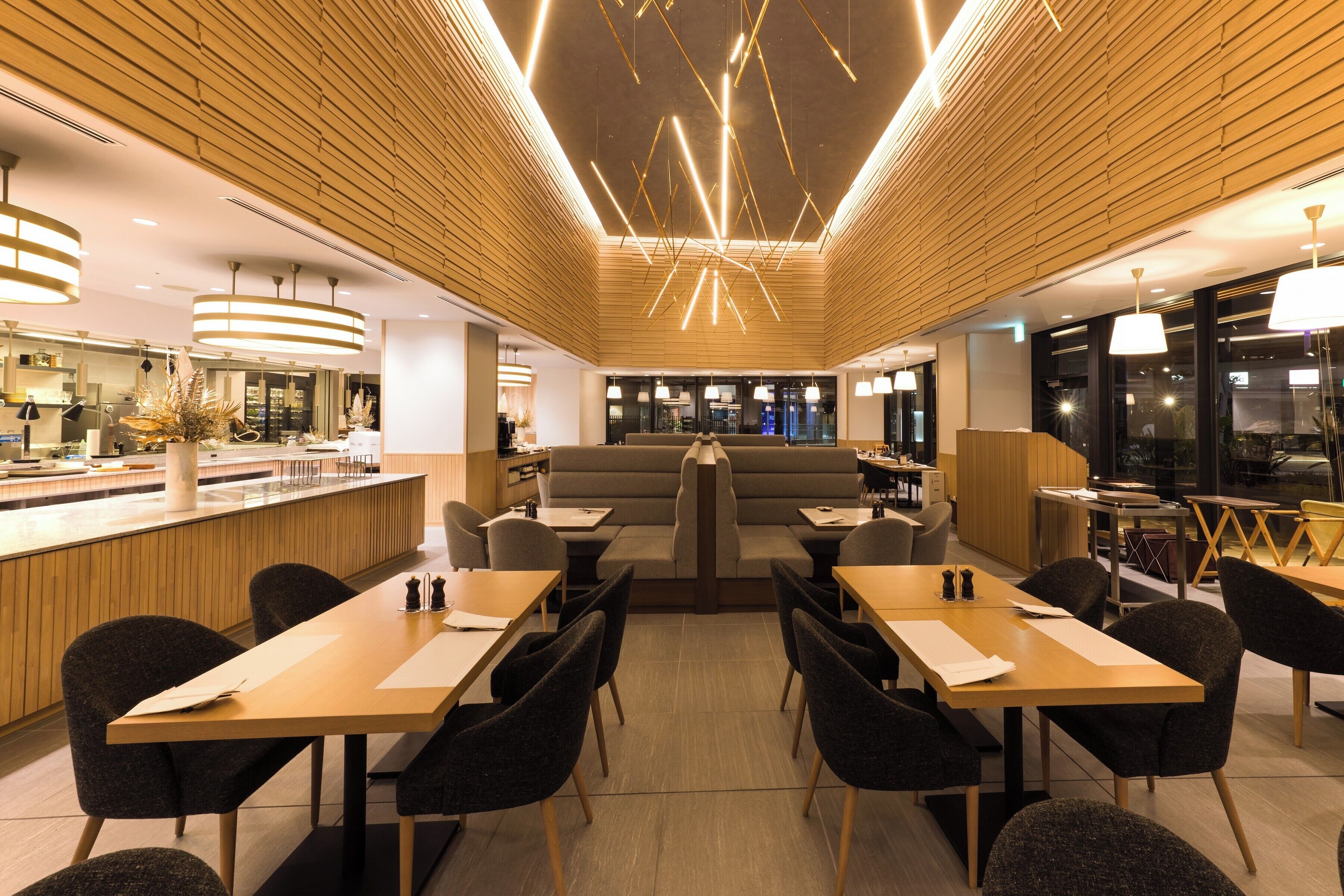 A modern restaurant with a central seating area, wooden paneling, and pendant lighting.