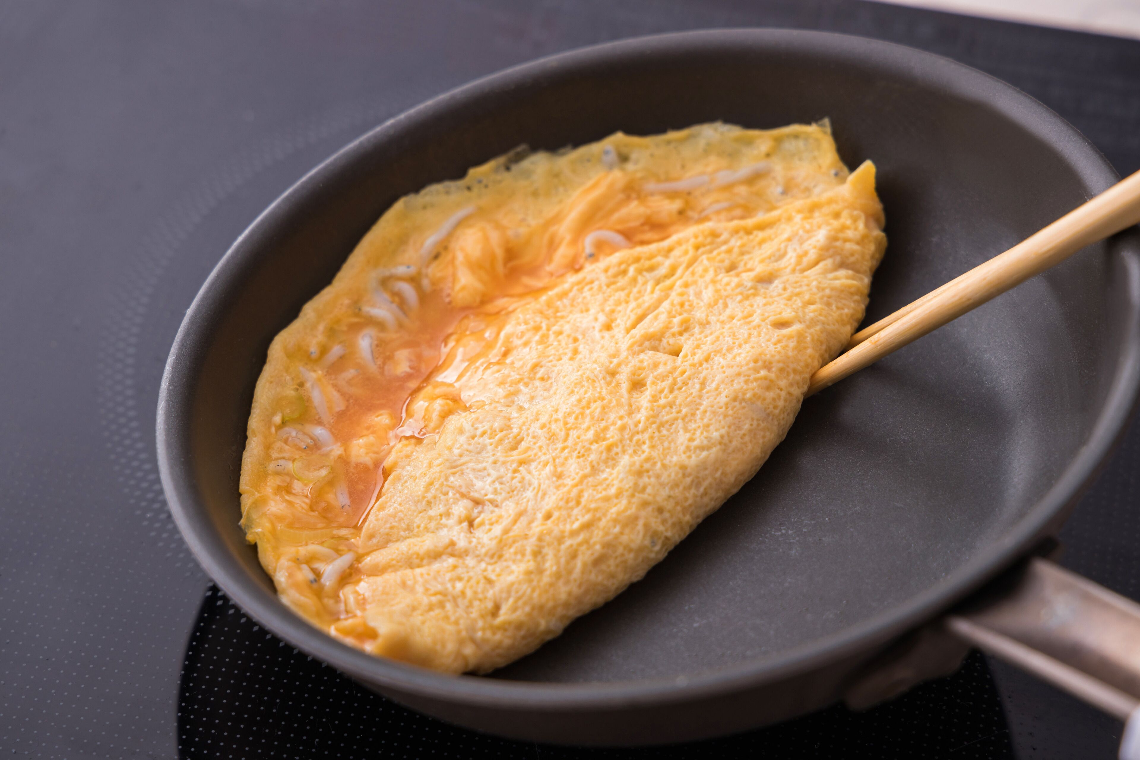 A pan with a folded omelette and chopsticks.