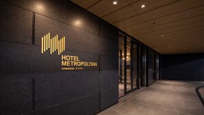 Een moderne hotelentree met een donkere gevel en een logo boven de naam 'HOTEL METROPOLITAN KAWASAKI JR-EAST'.