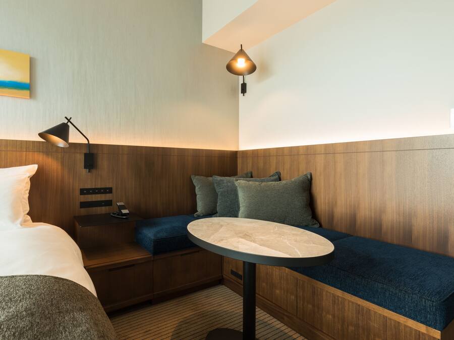 Habitación de hotel moderna con cama, una mesita redonda, un banco y una lámpara de pared.