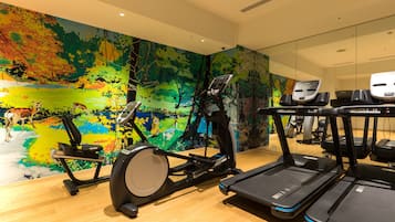 Un gimnasio con equipo de ejercicio y un mural colorido en la pared.