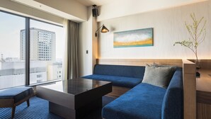 Een moderne hotelkamer met een groot raam, een blauwe bank, een kleine tafel en een schilderij aan de muur.