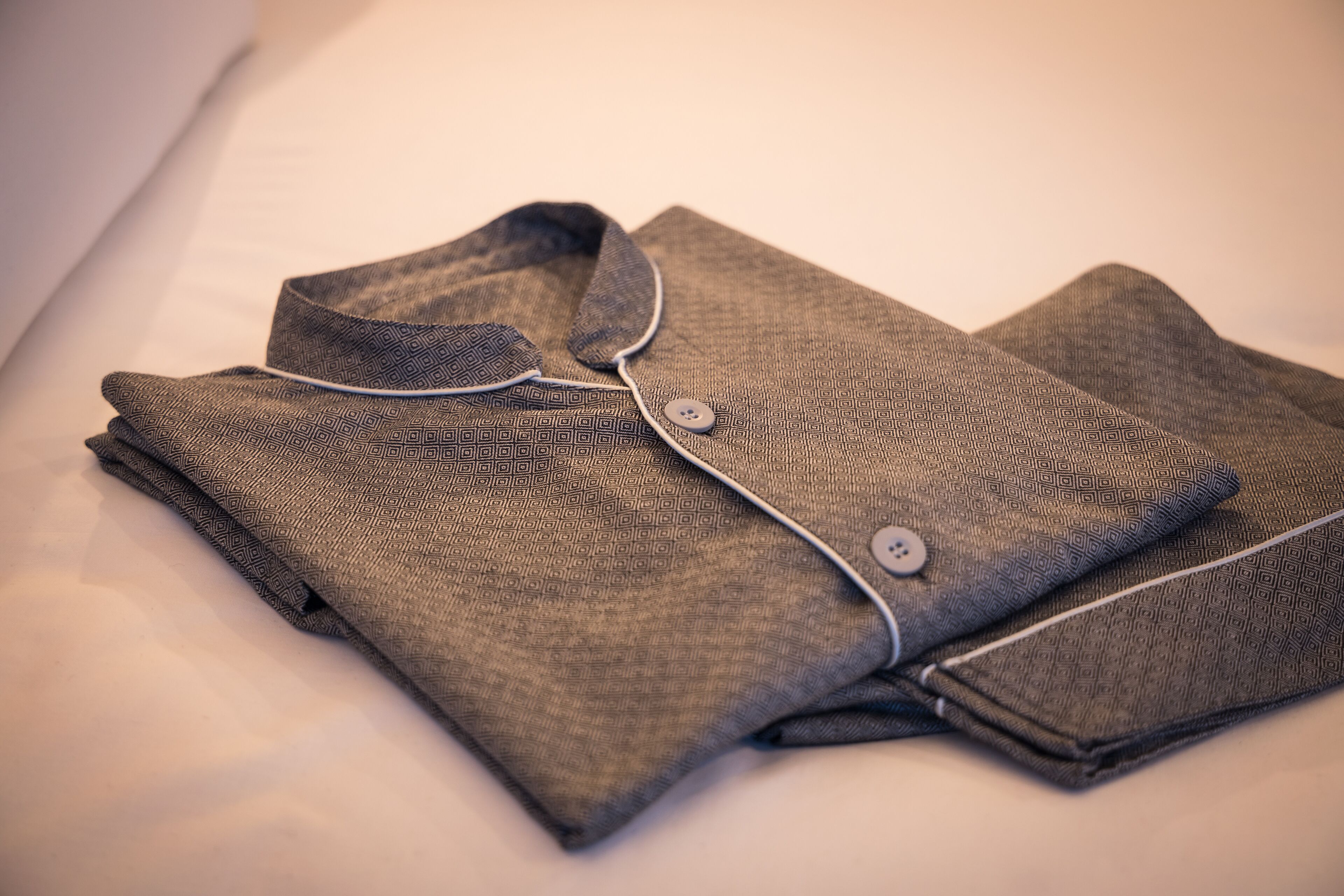 A neatly folded shirt with a button and a collar, placed on a bed.