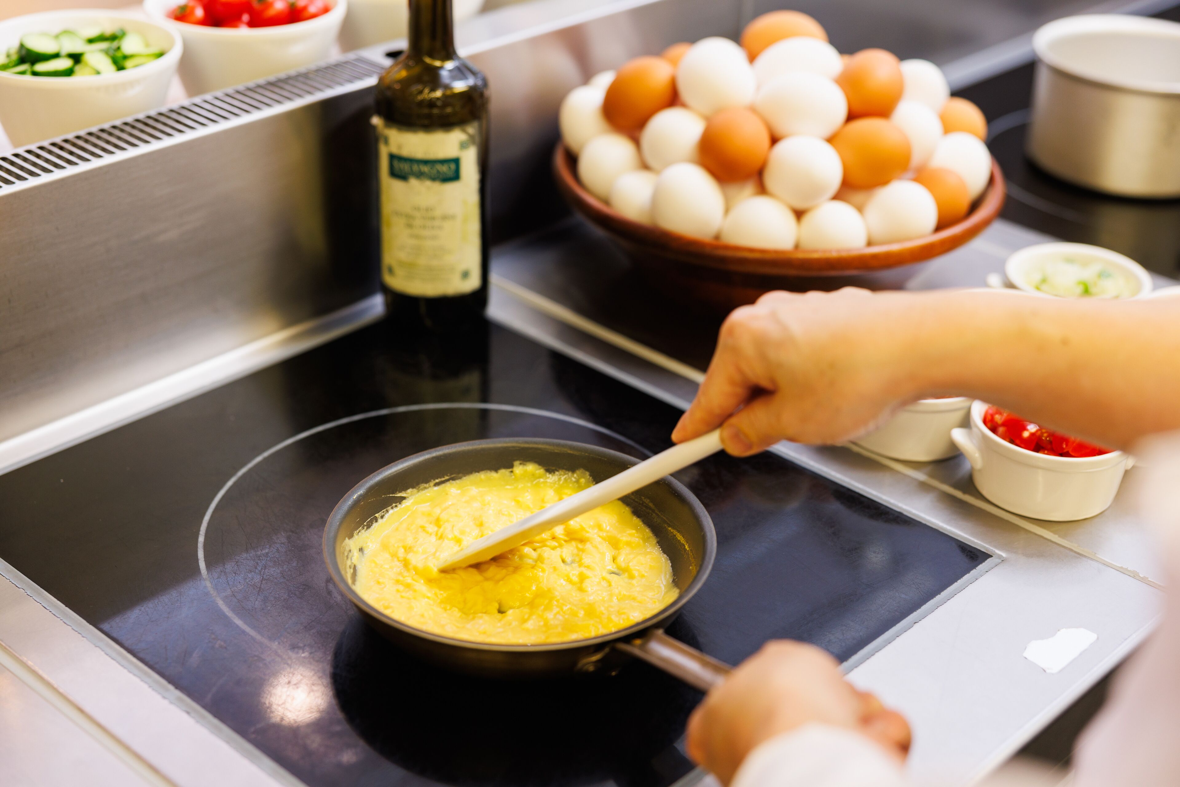 A kitchen with a frying pan on a stove, a bowl of eggs, and a bottle of oil.