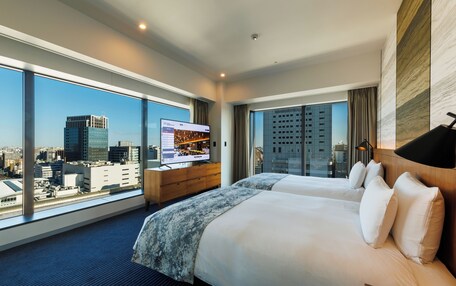 A hotel room with two beds, a TV, and a large window with a city view.