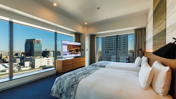 Een hotelkamer met twee bedden, een televisie en een groot raam met uitzicht op de stad.