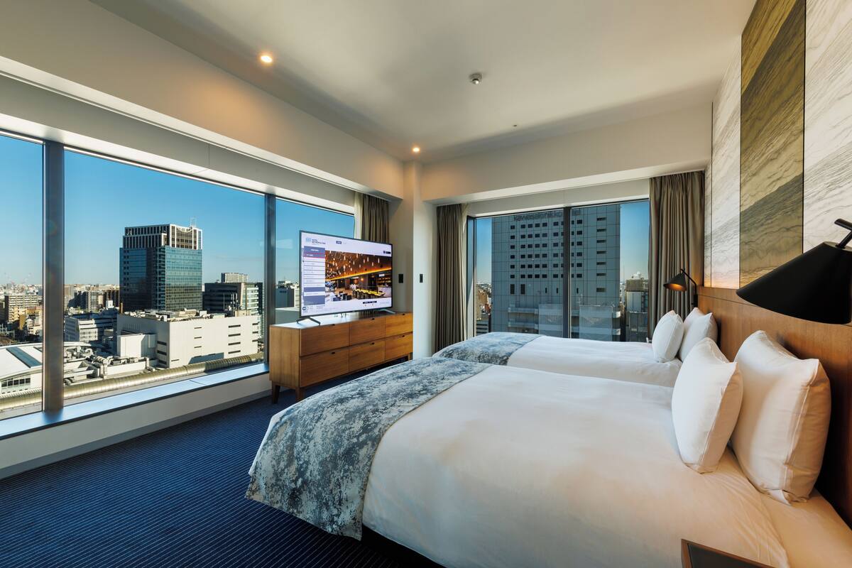 Een hotelkamer met twee bedden, een televisie en een groot raam met uitzicht op de stad.