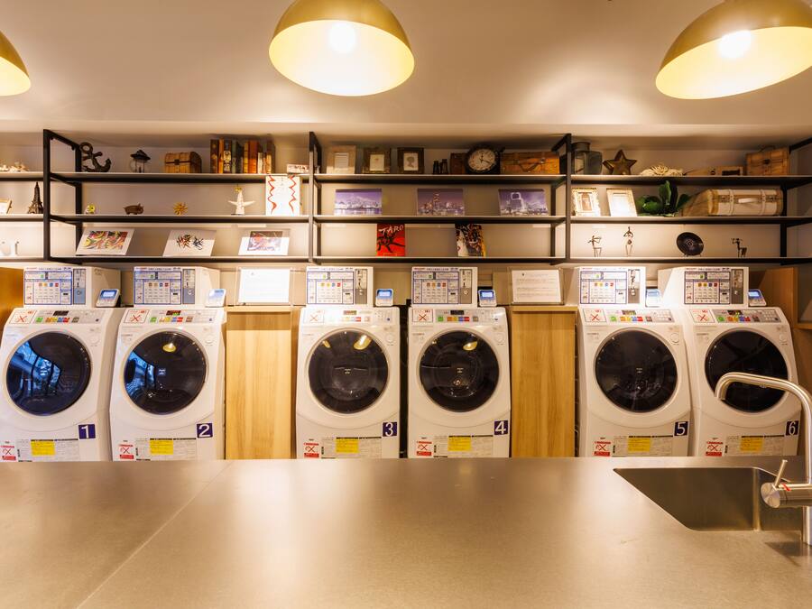 A laundry facility with six washing machines, a sink, and shelves with various items.