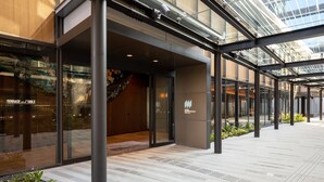 Een moderne hotelentree met glazen deuren, een zichtbaar bord met 'TERRACE and TABLE', en een overdekt buitenruimte met metalen pilaren.
