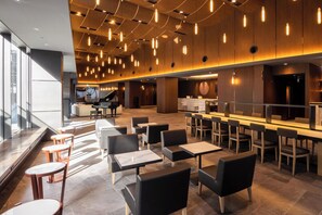 Un hall d’hôtel moderne doté d’un bar, de coins salon et d’un piano.