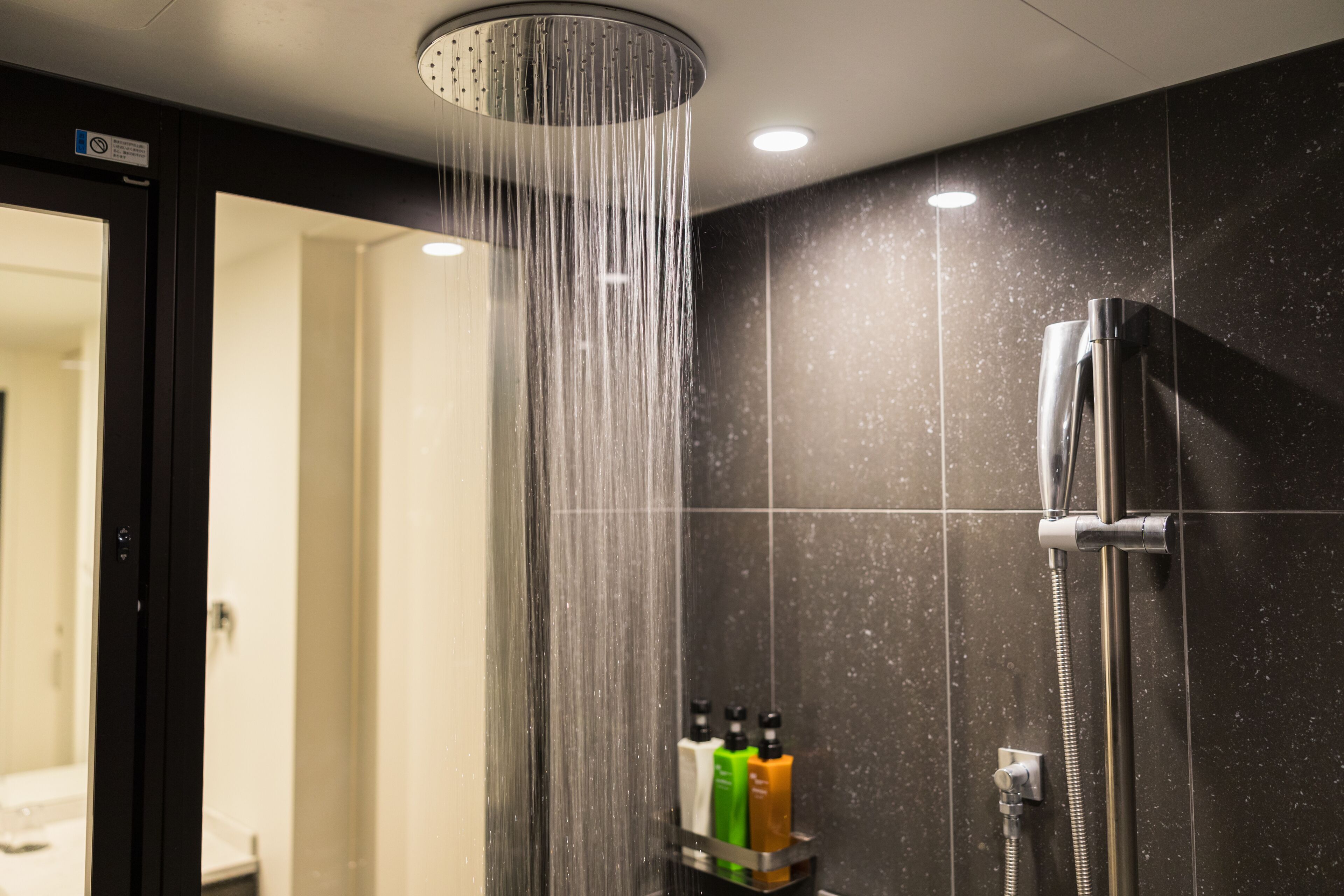 Ducha moderna con cabezal de ducha de lluvia, cabezal de ducha manual y portabotellas con artículos de aseo.