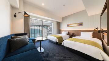Een hotelkamer met twee bedden, een sofa, een kleine tafel en een groot raam met uitzicht op een gebouw.
