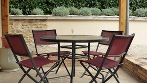 A round table with four chairs, set outdoors with a stone wall and greenery in the background. - Chambres sous les vignes du Buttois (Bussy-le-Grand)