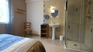 A bedroom with a bed, a chair, a bedside table, a small shelf, and a window with curtains. - Chambres sous les vignes du Buttois (Bussy-le-Grand)