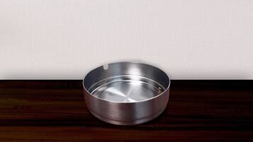 A metallic ashtray on a wooden surface against a plain wall.