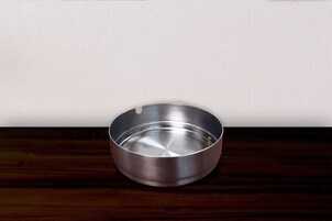 A metallic ashtray on a wooden surface against a plain wall.
