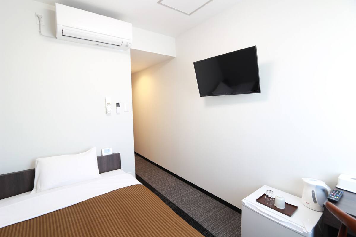 Quarto de hotel com cama, TV de tela plana na parede, cafeteira e uma mesinha com bandeja.