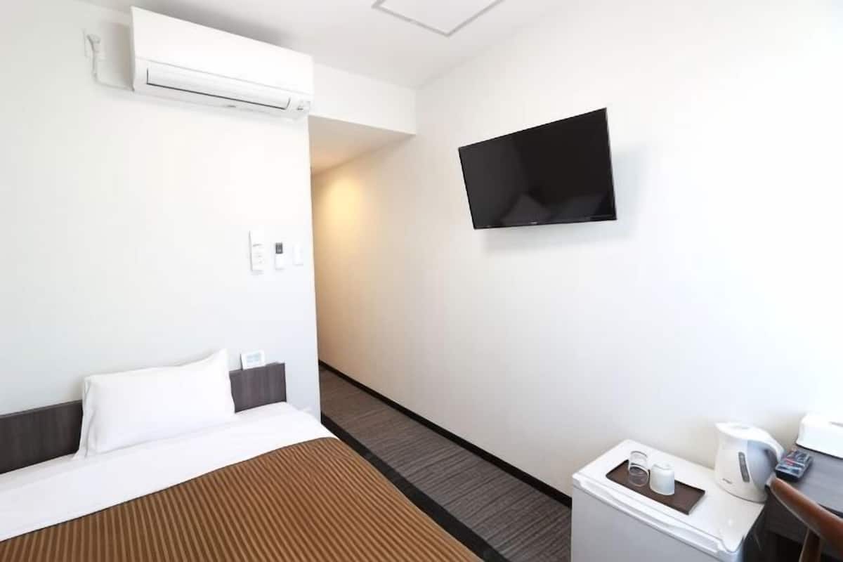 Quarto de hotel com uma cama, televisão de tela plana, cafeteira e uma mesa pequena com uma xícara e um controle remoto.
