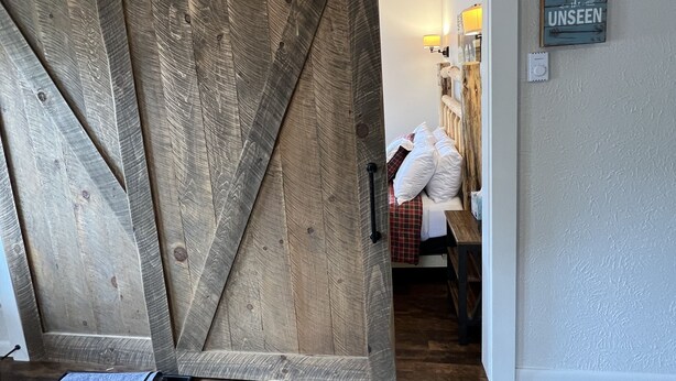 Ein Zimmer mit einer Holztür im Scheunenstil, einem Bett mit karierter Decke und einem an der Wand befestigten Schild.