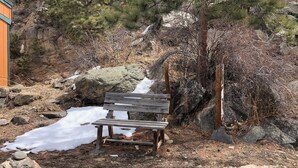 Eine Holzbank inmitten felsiger Landschaft mit Kiefern und vereinzelten Schneeflecken.