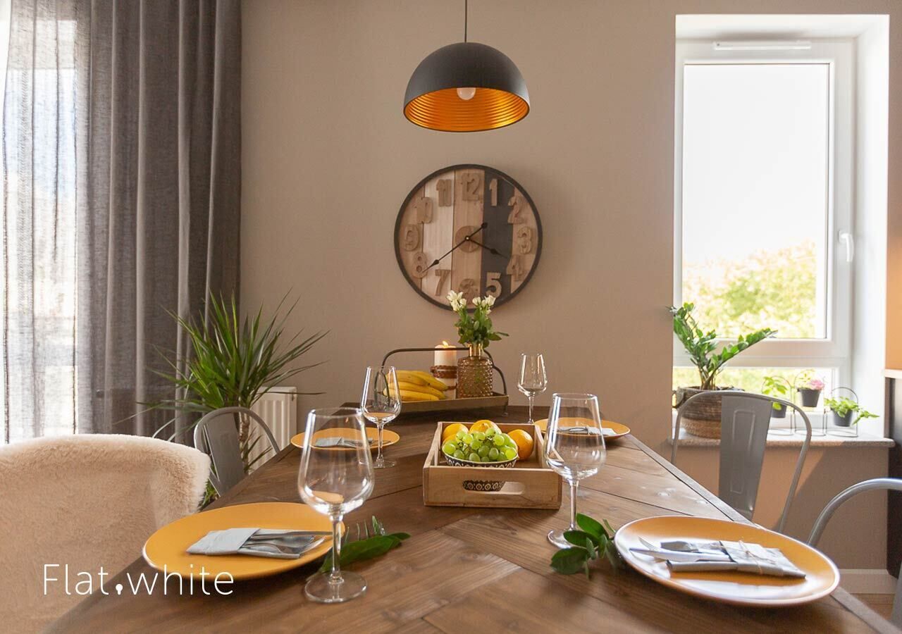 Un comedor con una mesa de madera dispuesta para dos personas, un reloj en la pared y una lámpara colgante.