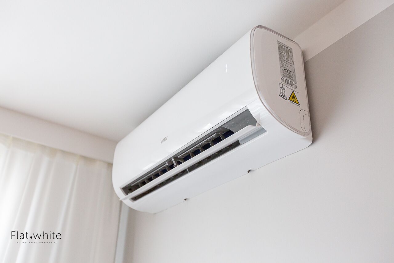 Eine weiße Klimaanlage ist an einer Wand in einem Raum mit weißen Vorhängen befestigt.