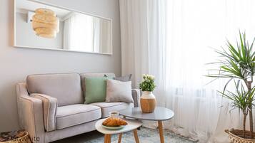 A modern living room with a grey sofa, a small round table, a potted plant, and a large mirror on the wall.