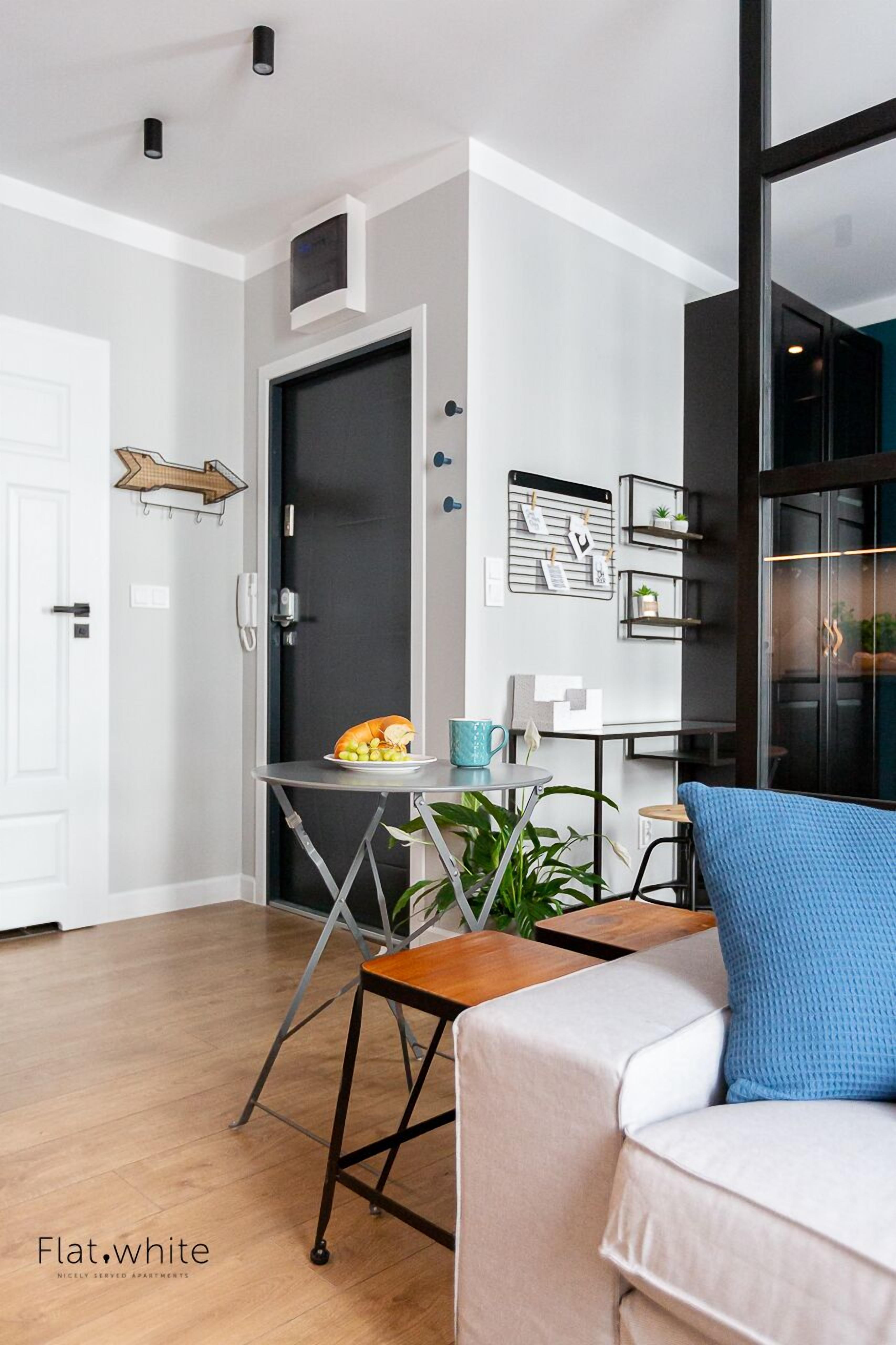 A modern living room with a sofa, a small table with a plant, and a door with a black frame.