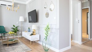 A modern living room with a flat-screen TV, a white console table, a green chair, and a glass vase with plants. - Flat White Apartamenty Obywatelska 47 (Zielona Gora)