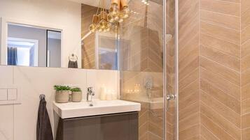 Une salle de bain moderne avec une douche à l’italienne en verre, un meuble-lavabo et un lustre.