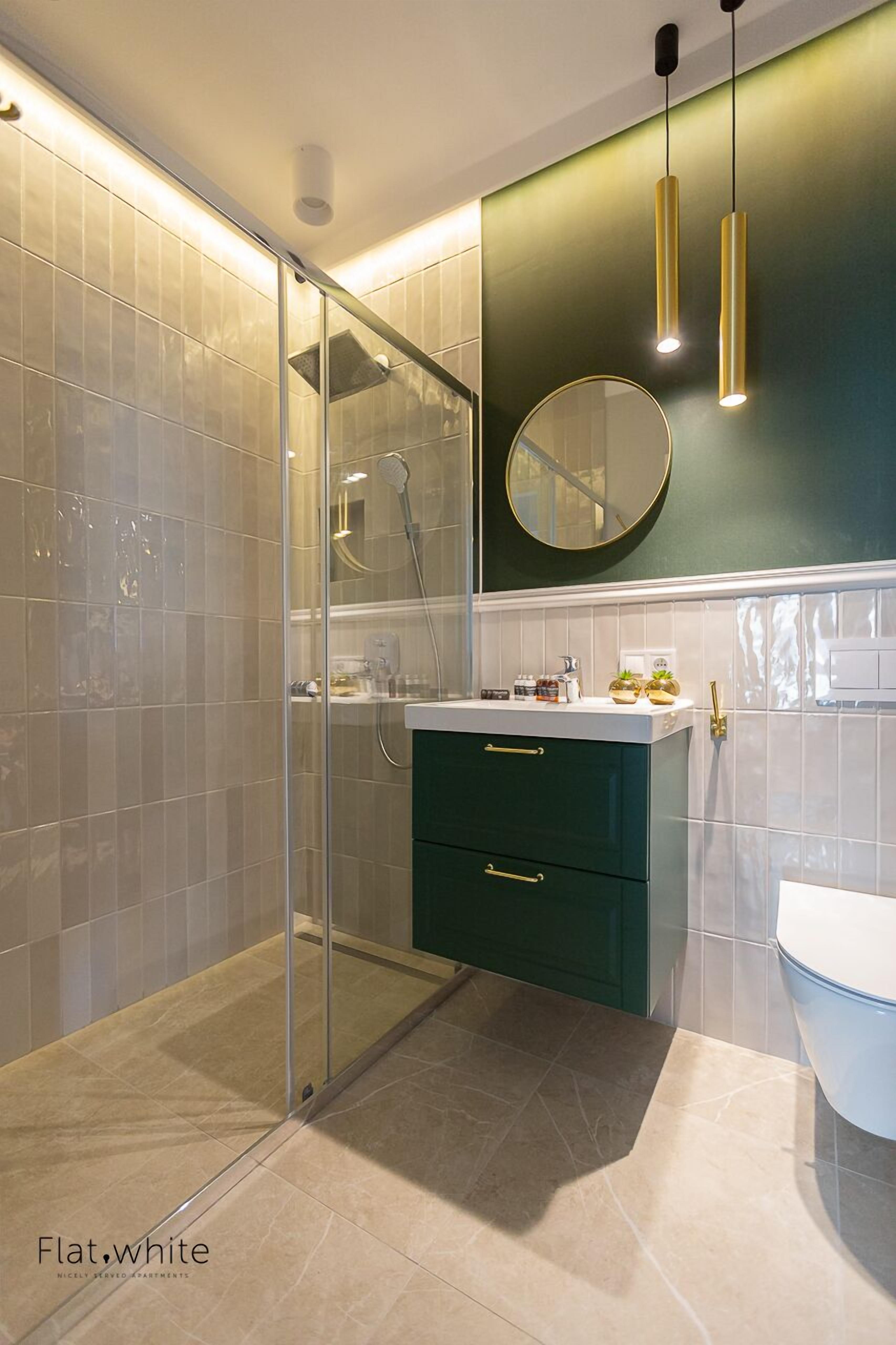 Een moderne badkamer met een douchecabine van glas, een groen badkamermeubel en een ronde spiegel.