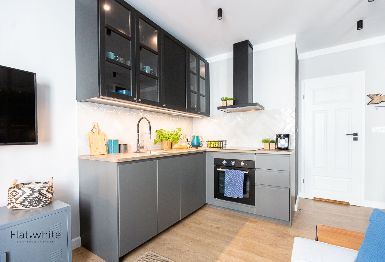 A modern kitchen with grey cabinets, a built-in oven, and a coffee machine.