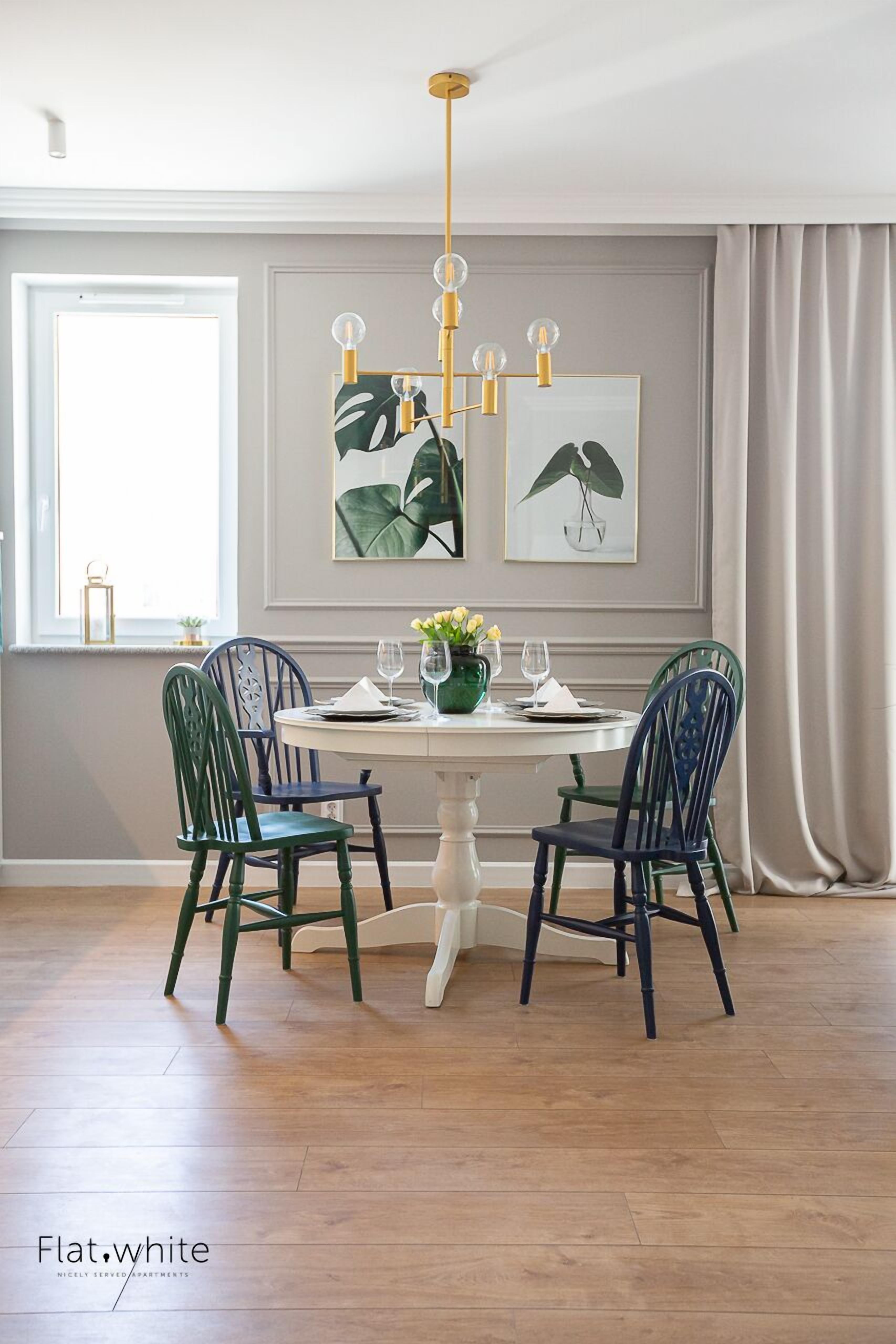 Uma sala de jantar com uma mesa redonda, quatro cadeiras, um vaso com flores e obras de arte emolduradas na parede.