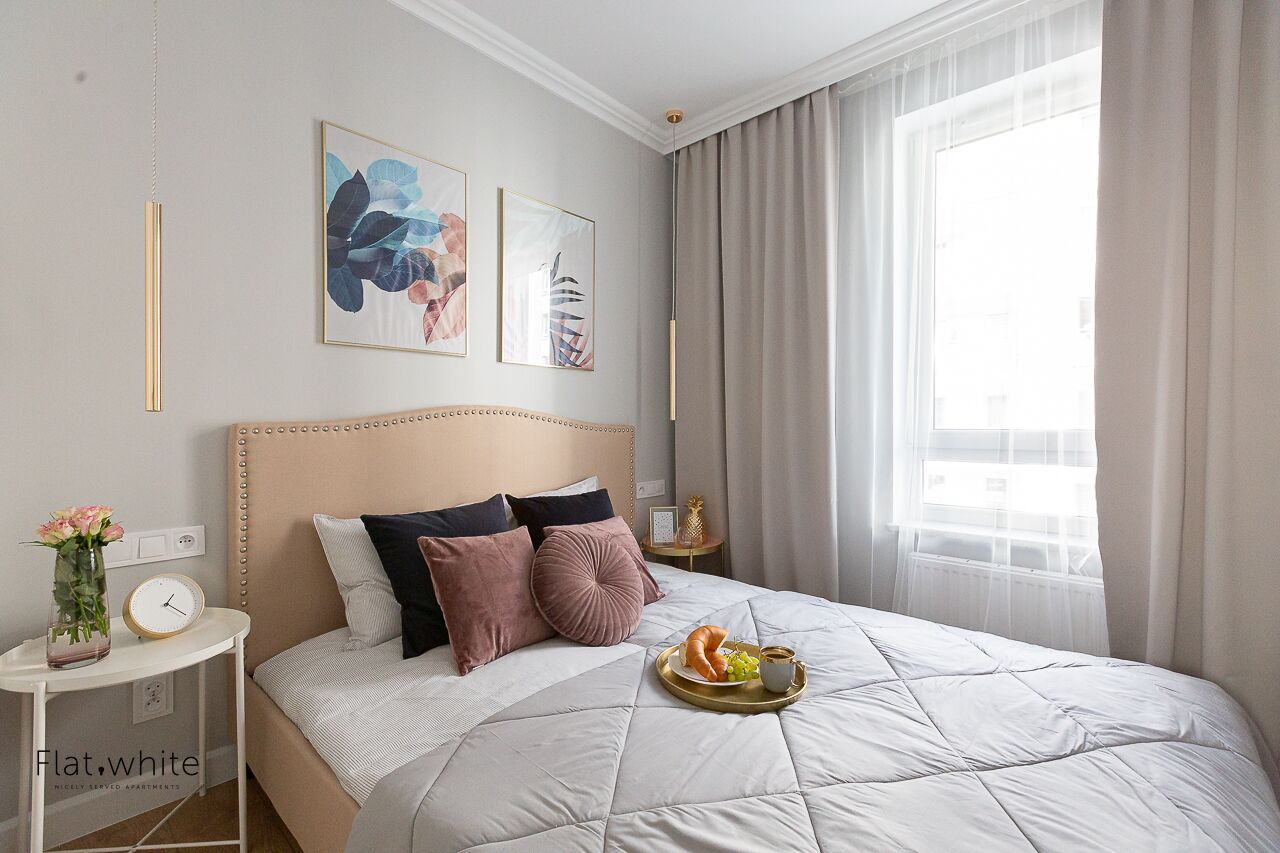 A neatly arranged bedroom with a large bed, a bedside table with a clock and vase, and artwork on the wall.