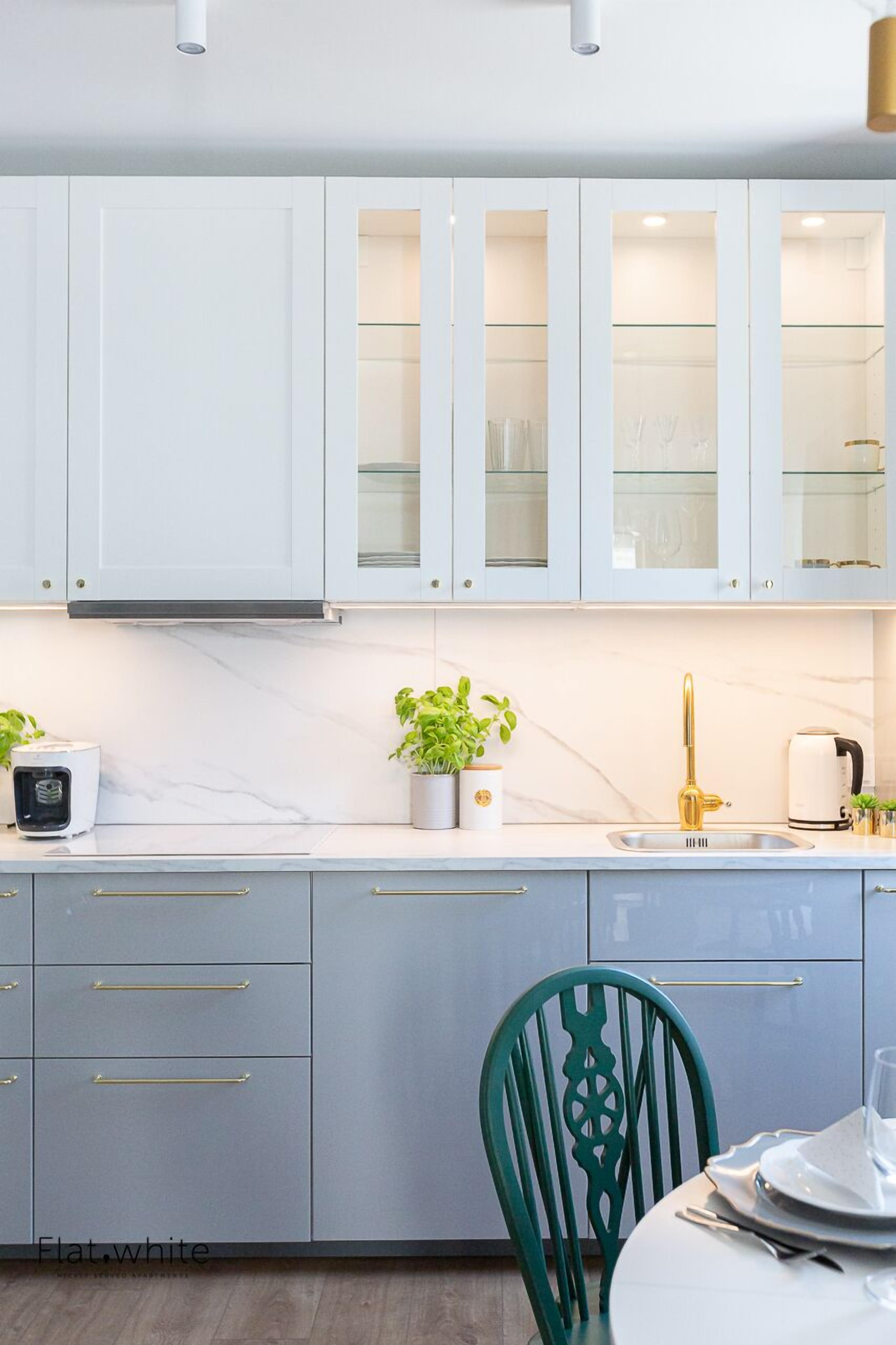 A modern kitchen with white cabinets, a marble countertop, and a green chair.
