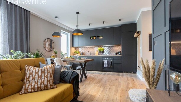 A modern kitchen with dark cabinets, a wooden dining table, and pendant lighting. - Flat White Apartamenty Obywatelska 47 (Zielona Gora)