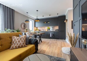 A modern kitchen with dark cabinets, a wooden dining table, and pendant lighting. - Flat White Apartamenty Obywatelska 47 (Zielona Gora)