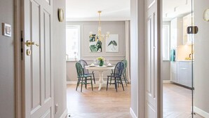 A hallway with a dining area in the background, featuring a table and chairs, and a kitchen area visible through an open door. - Flat White Apartamenty Obywatelska 47 (Zielona Gora)