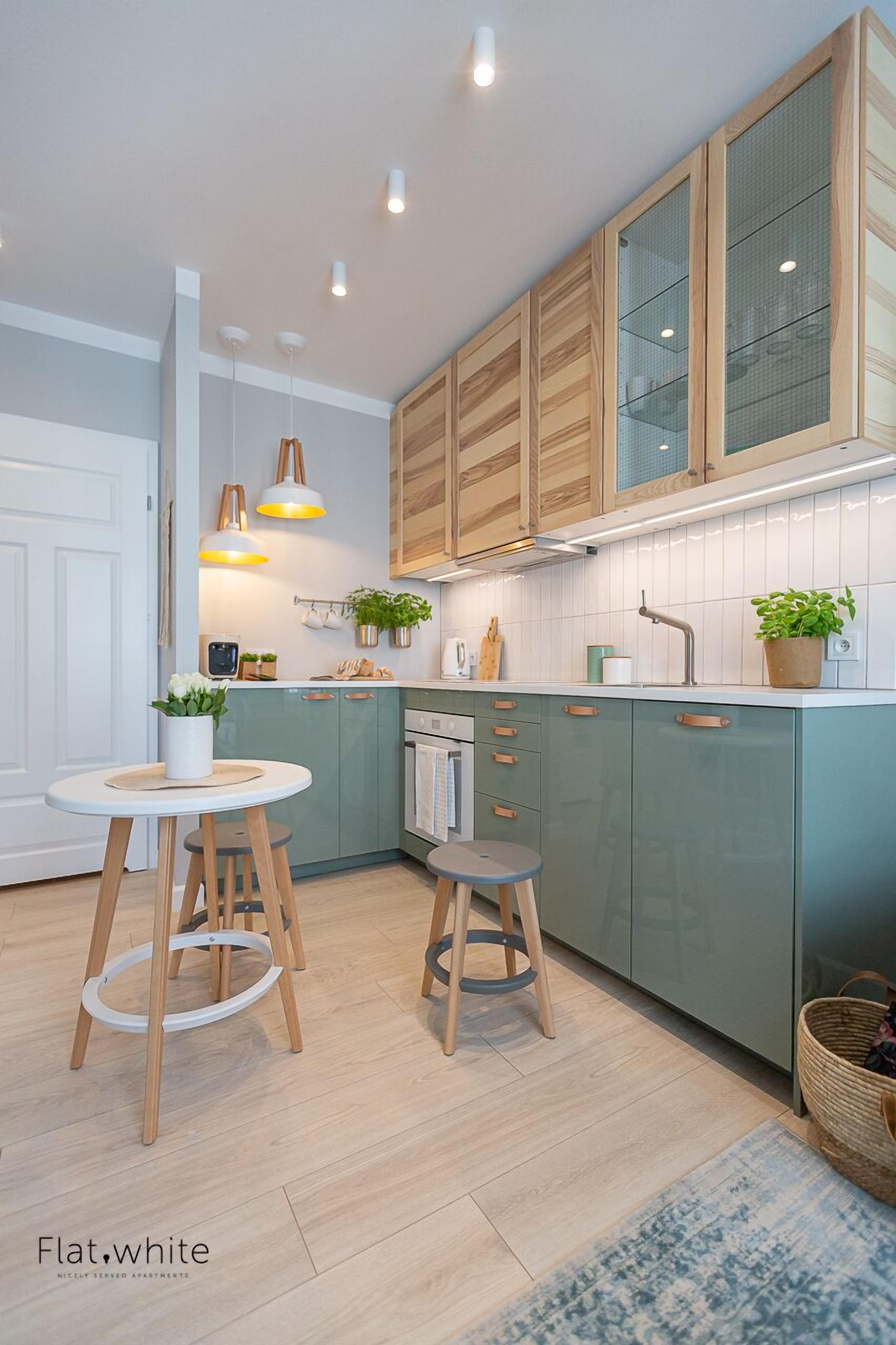 A modern kitchen with green cabinets, wooden stools, and pendant lighting.