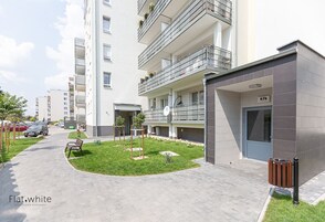 Un moderno edificio de apartamentos con un patio central, un banco y un contenedor de basura.