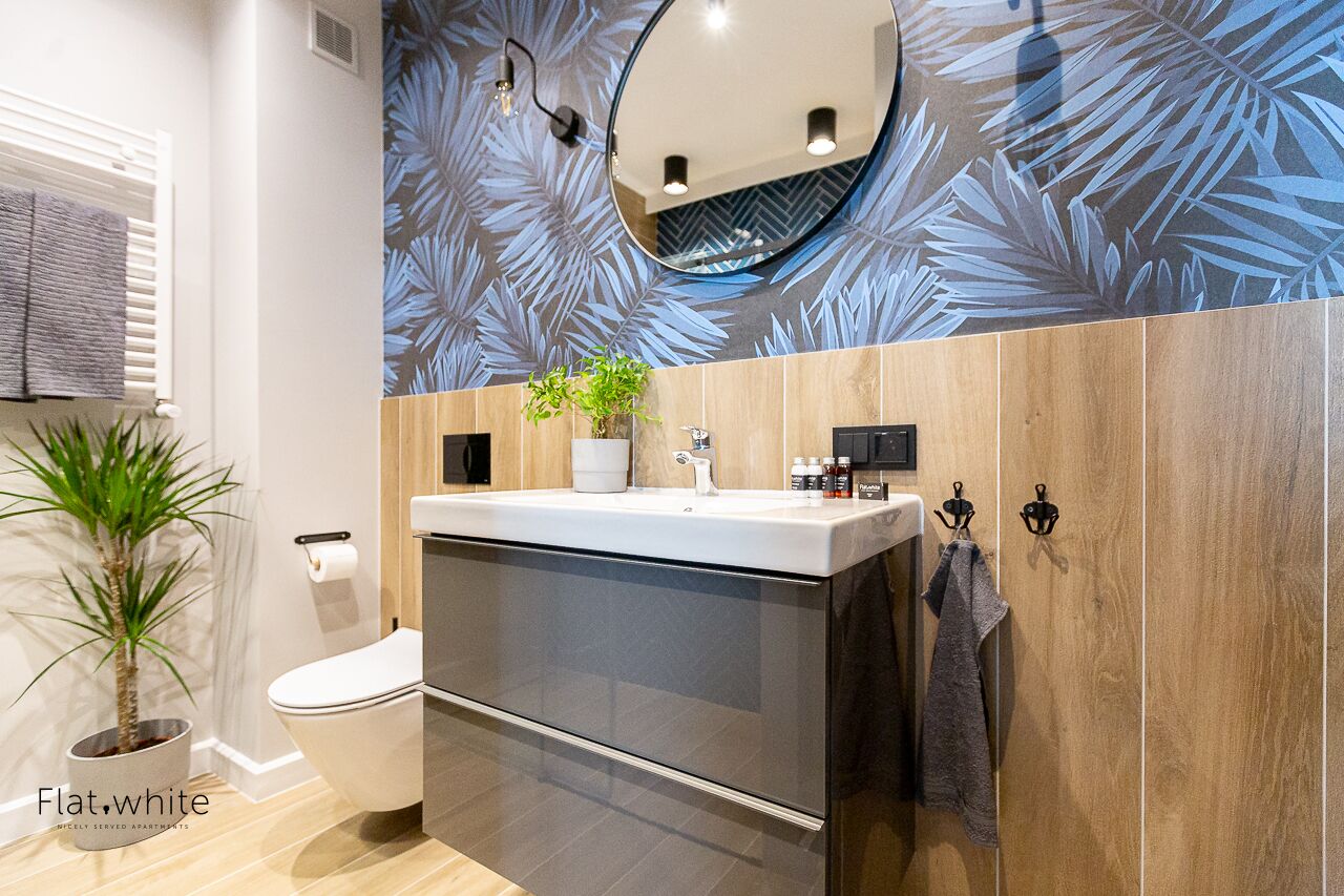 A modern bathroom with a toilet, sink, and mirror. There is a potted plant and a towel rack.