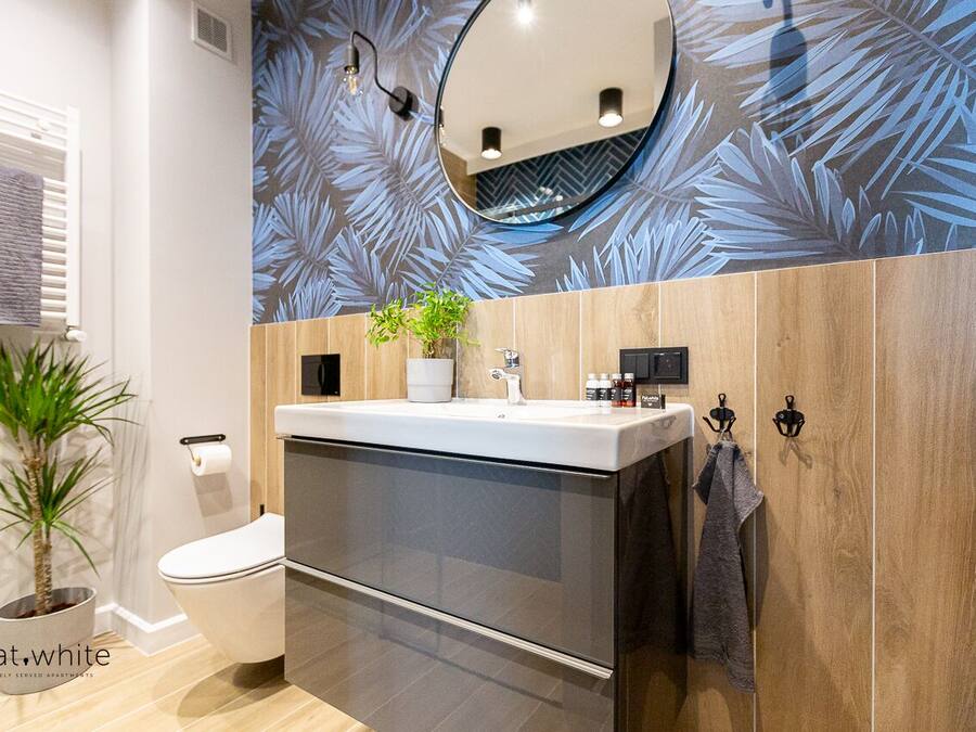 A modern bathroom with a toilet, sink, and mirror. There is a potted plant and a towel rack.