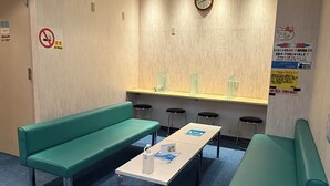 Zona d'espera amb seients verds, taula amb ampolla d'aigua i fulletons, rellotge a la paret i senyalitzador de prohibició de fumar.