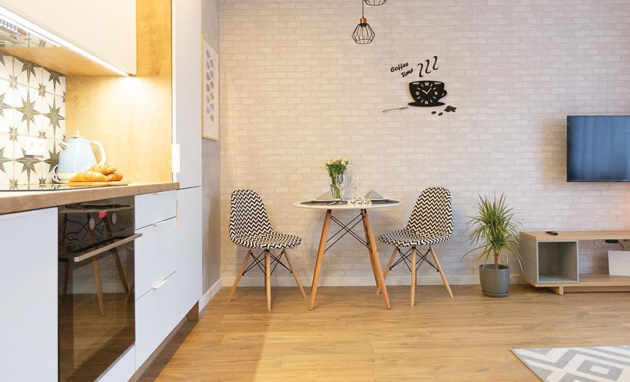 A modern kitchen with a dining area, featuring a white brick wall, a clock, and a TV.