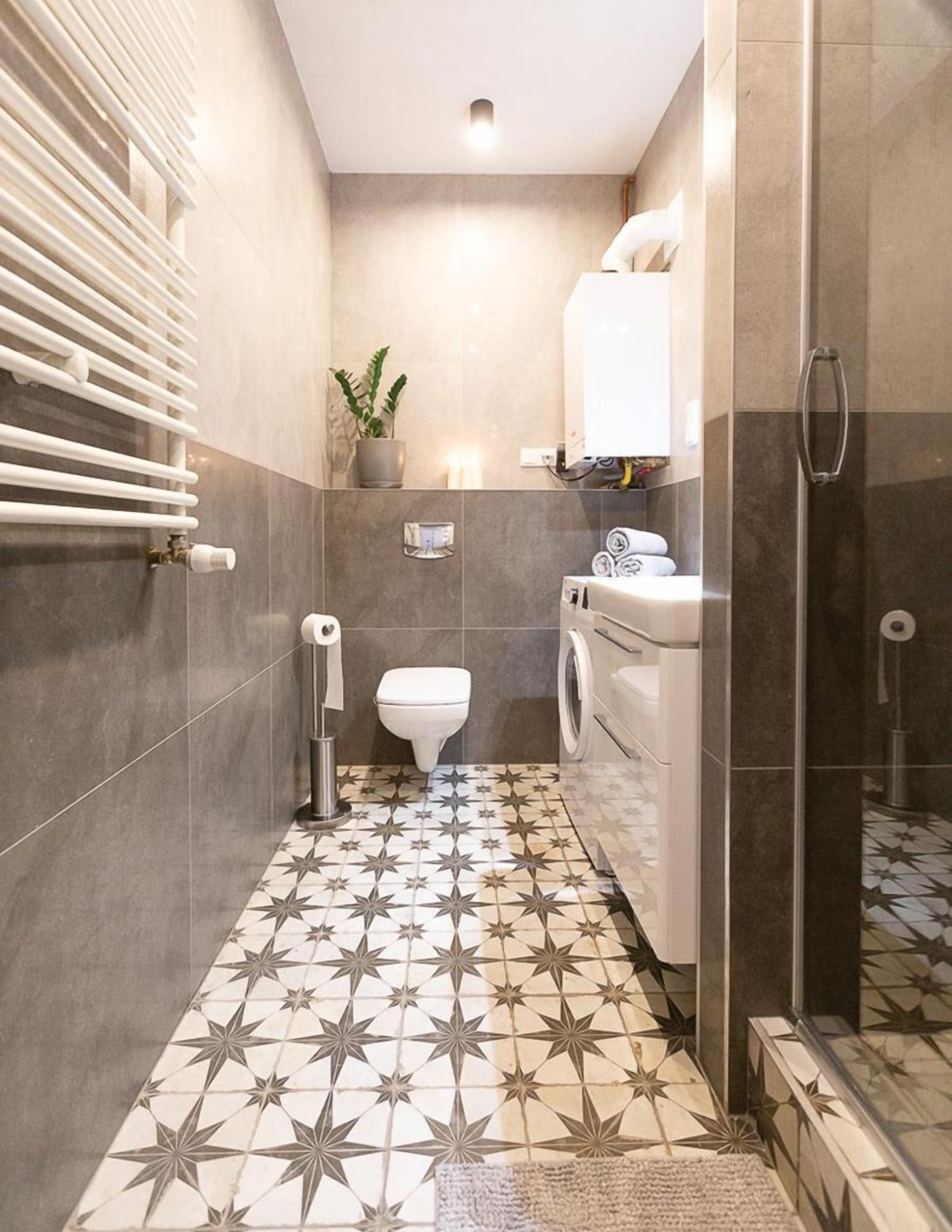 A compact bathroom with a star-patterned floor, a toilet, a washing machine, and a towel rack.