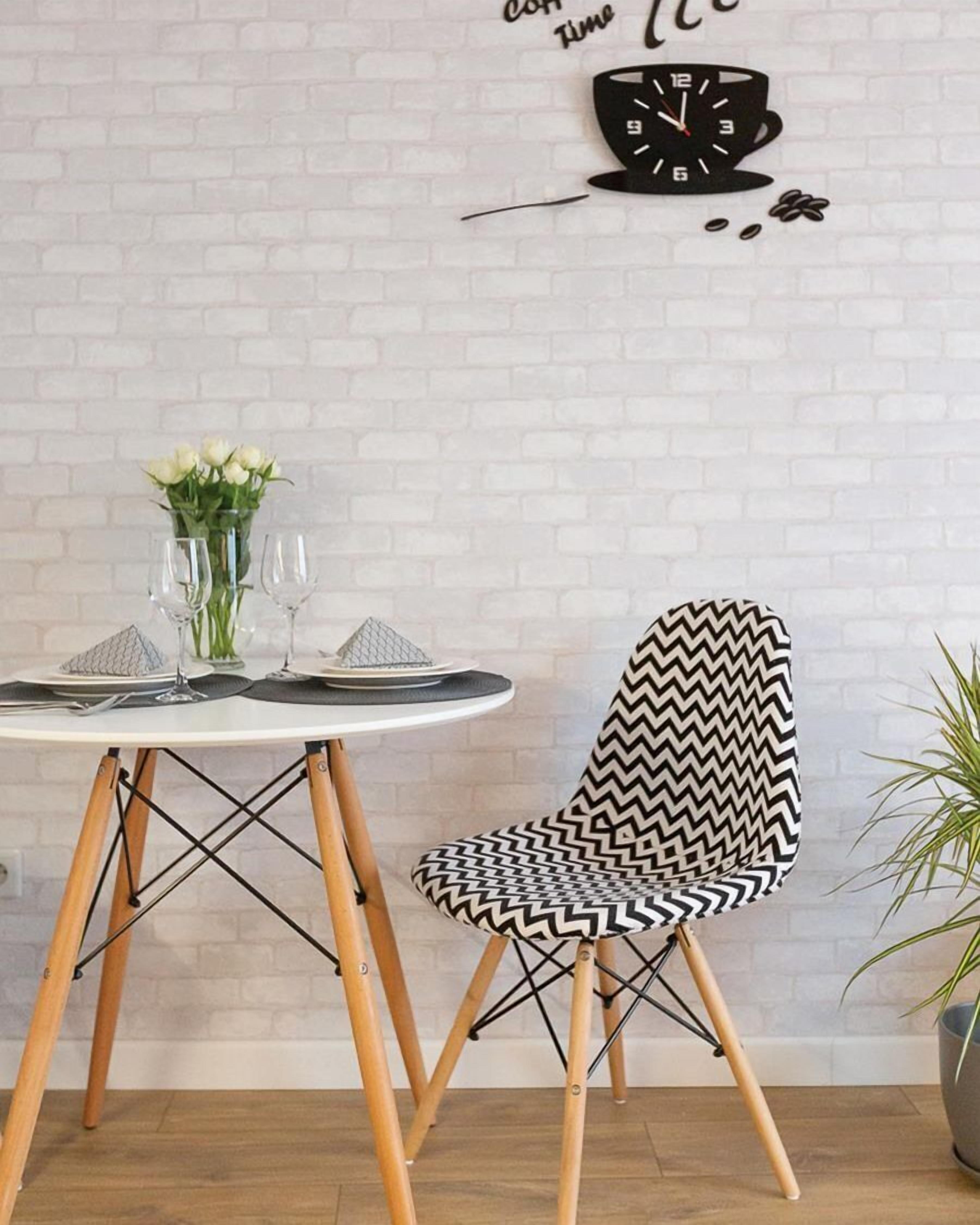 Un coin repas avec une table ronde dressée pour deux personnes, une chaise à motifs zigzag noir et blanc et une horloge murale au-dessus de la table.