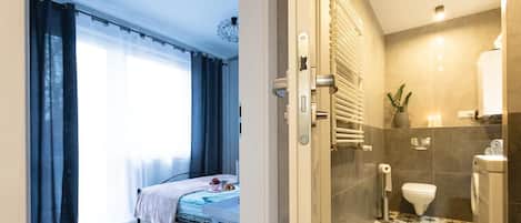 A bedroom with a bed, a window with curtains, and a bathroom with a toilet, sink, and towel rack.