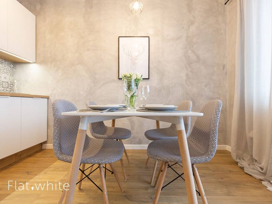 Un comedor con una mesa blanca y sillas estampadas, un cuadro en la pared y un jarrón con plantas.