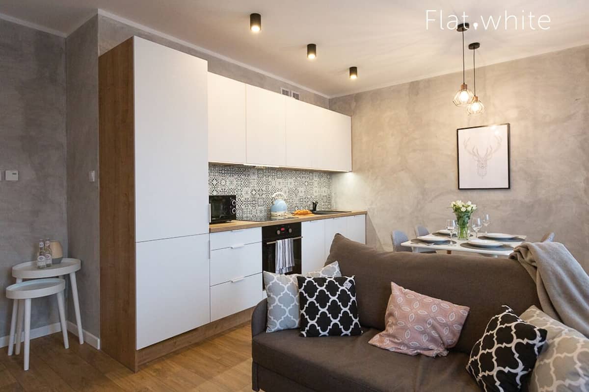 Une cuisine moderne avec des meubles blancs, un plan de travail en bois et un coin repas avec une table dressée pour deux personnes.
