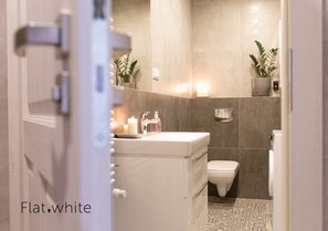 Un baño moderno con un lavamanos blanco, un inodoro y un estante empotrado con plantas.